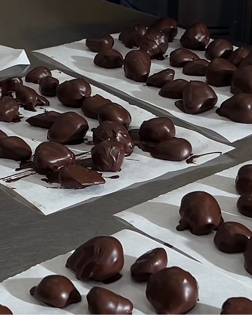 Several trays of chocolate-covered confection pieces arranged on white parchment paper in a production setting.